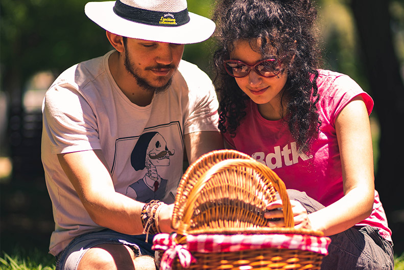 Couple sitting down opening up picnic basket. 