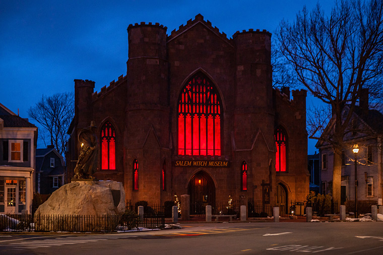 A New England-style church building illuminated with eerie orange light from within, set against the dusk sky.