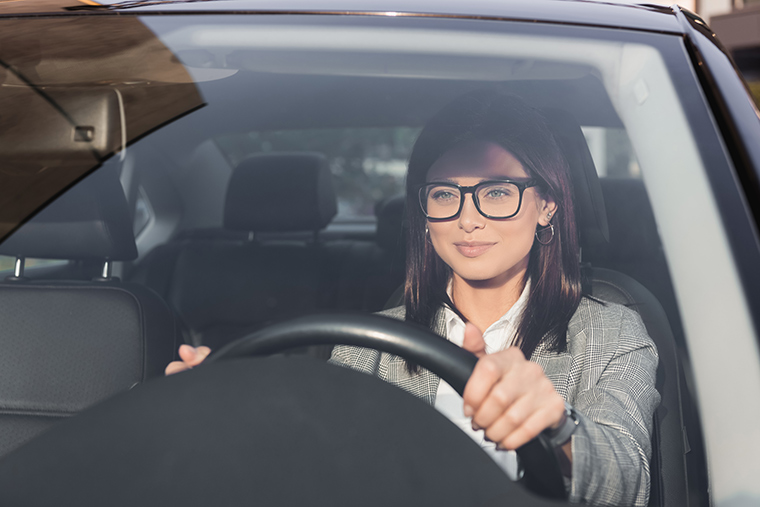 Close-up photo of a dynamic young professional woman behind the wheel, driving confidently.
